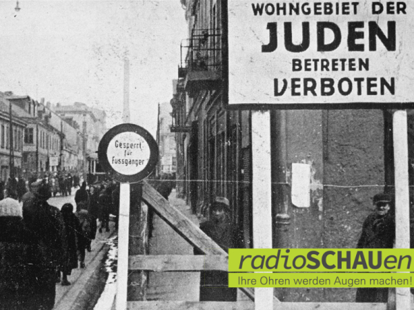 Historische Fotografie, die den Eingang zum jüdischen Ghetto der polnischen Stadt Lodz zeigt. Rechts oben im Vordergrund ist ein großes Schild zu sehen, auf dem steht: "Wohngebiet der Juden, betreten verboten": 